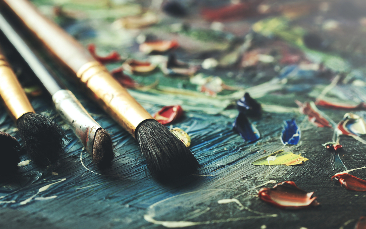 Pinsel liegen auf einer Leinwand mit verschiedenen Farbflecken und Farbtupfern.