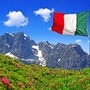 Italienische Flagge weht vor Bergkulisse mit Blumenwiese.