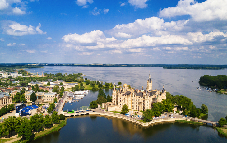 Luftaufnahme eines Schlosses am Wasser unter blauem Himmel und Wolken.