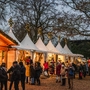 Weihnachtsmarkt mit Verkaufsständen und Menschen unter beleuchteten Bäumen.