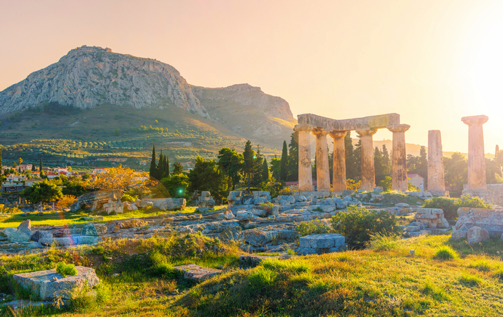 Ruinen eines antiken Tempels vor einer Berglandschaft bei Sonnenuntergang.