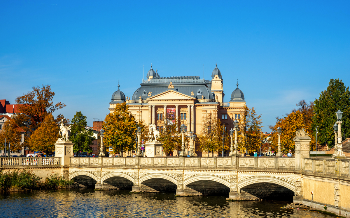 Theatergebäude hinter Fluss mit Brücke an einem sonnigen Herbsttag.