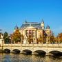 Theatergebäude hinter Fluss mit Brücke an einem sonnigen Herbsttag.