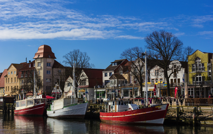 Fischerboote im Hafen vor historischen Gebäuden, klarer Himmel im Hintergrund.