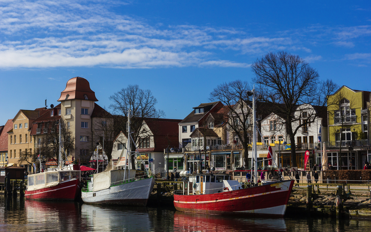 Fischerboote im Hafen vor historischen Gebäuden, klarer Himmel im Hintergrund.