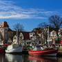 Fischerboote im Hafen vor historischen Gebäuden, klarer Himmel im Hintergrund.