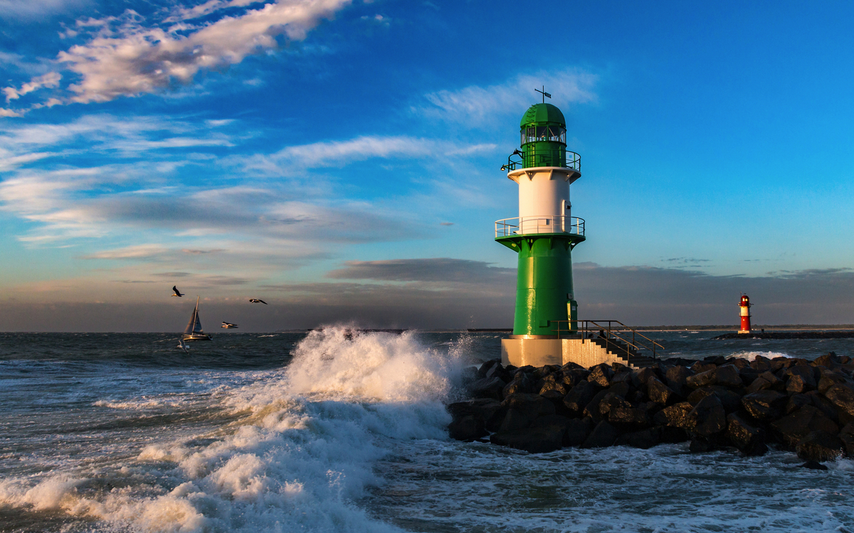 Leuchtturm an einer felsigen Küste bei Wellengang und blauem Himmel