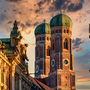 Frauenkirche in München bei Sonnenuntergang mit malerischem Himmel und Gebäudefassaden im Vordergrund.