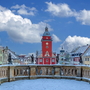 Marktplatz mit rotem Turmgebäude, umgeben von bunten Häusern im Winter.