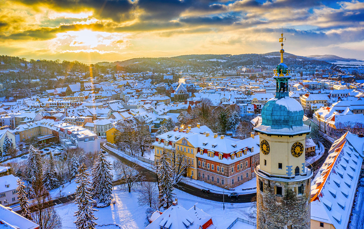 Verschneite Stadtlandschaft bei Sonnenaufgang mit Kirchturm im Vordergrund.
