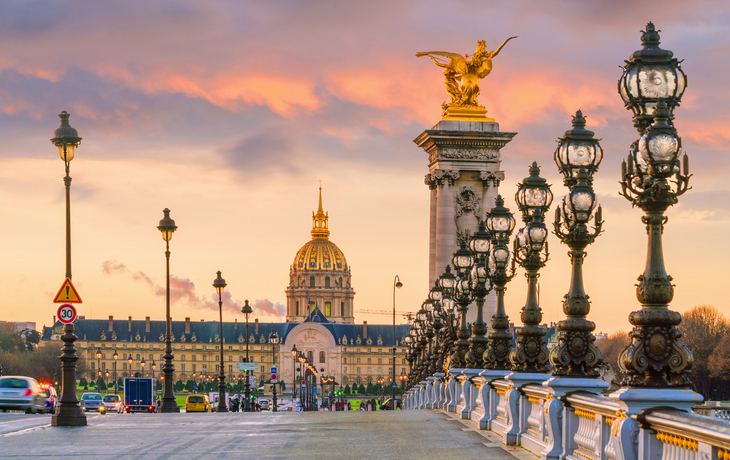 Blick auf die Pont Alexandre III in Paris bei Sonnenuntergang mit Les Invalides im Hintergrund.
