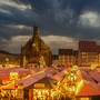 Abendlicher Weihnachtsmarkt mit beleuchteten Ständen und gotischer Kirche im Hintergrund.