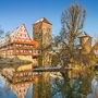 Fachwerkhaus und Brücke an einem Fluss im Winter, mit blauem Himmel im Hintergrund.