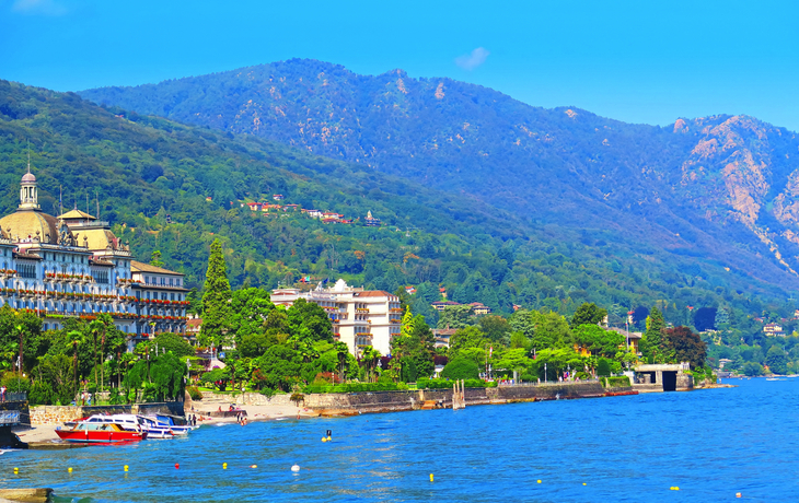 Landschaft mit Bergen, See und Gebäuden unter blauem Himmel.