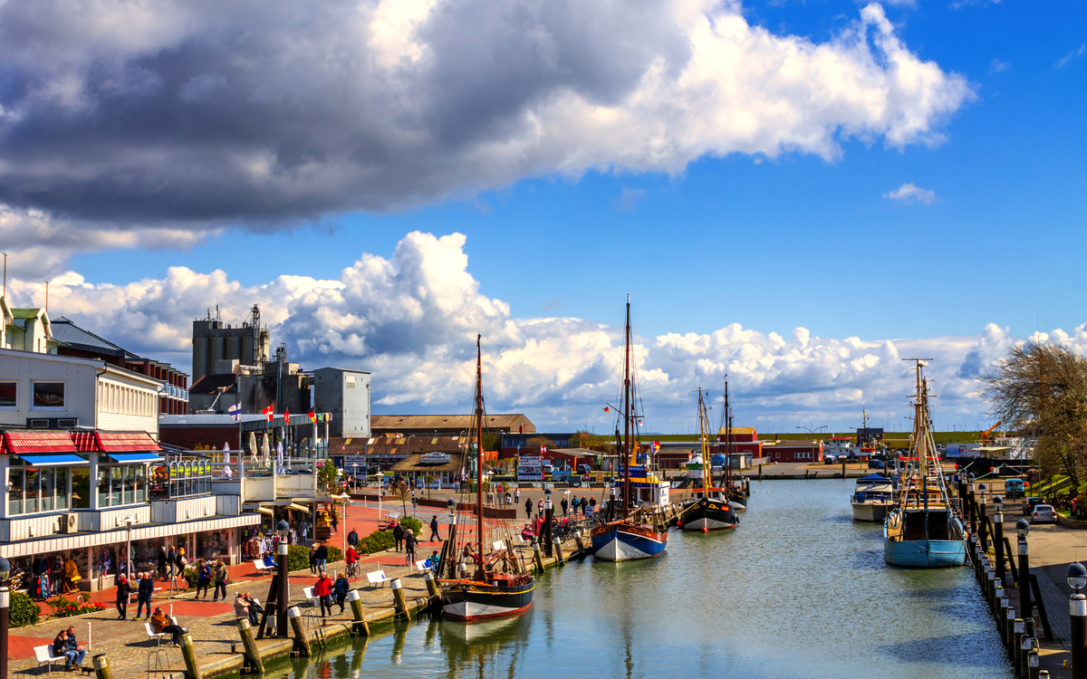 Hafen mit Booten, Gebäuden und Promenade unter wolkigem Himmel