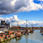Hafen mit Booten, Gebäuden und Promenade unter wolkigem Himmel