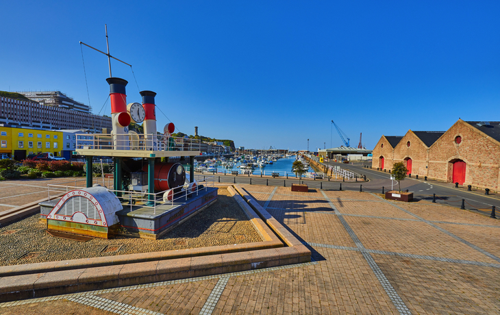 Hafenpromenade mit Schiff, Lagerhäusern und klarem Himmel.