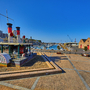Hafenpromenade mit Schiff, Lagerhäusern und klarem Himmel.