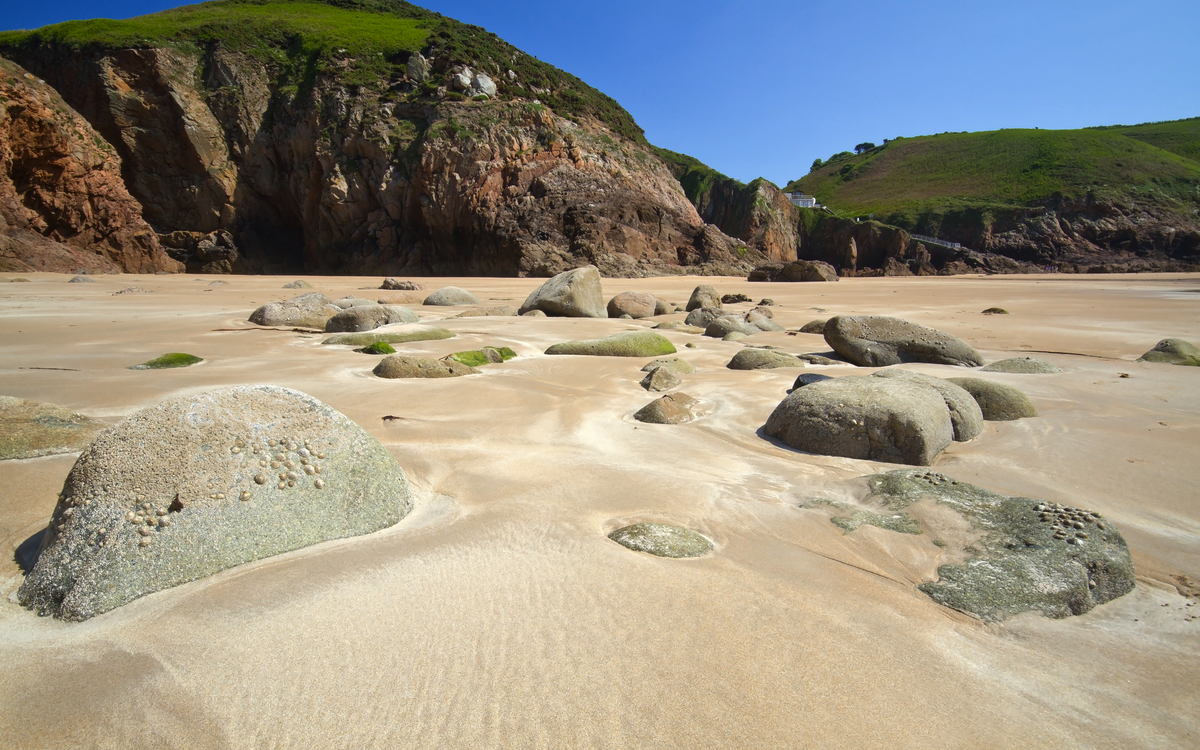 Felsen auf einem Sandstrand mit grünen Klippen im Hintergrund.
