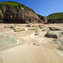 Felsen auf einem Sandstrand mit grünen Klippen im Hintergrund.