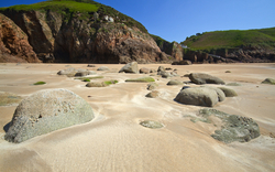 Felsen auf einem Sandstrand mit grünen Klippen im Hintergrund.