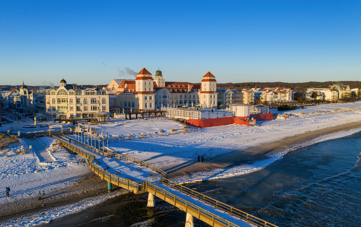 Winterlicher Strand mit Seebrücke und Gebäuden im Hintergrund bei Sonnenuntergang.