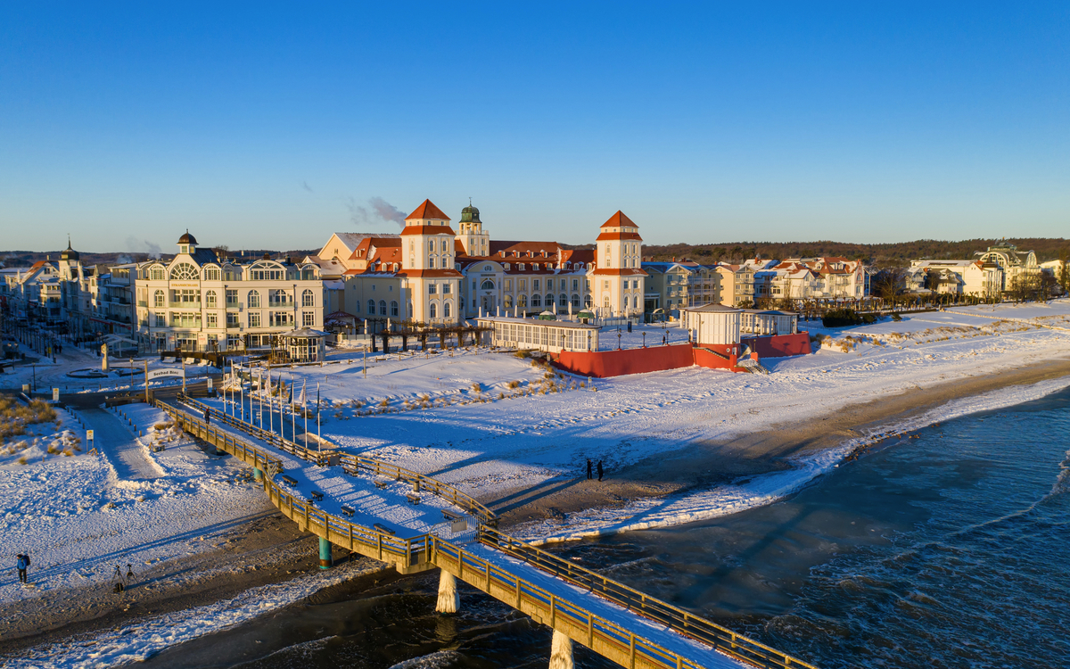 Winterlicher Strand mit Seebrücke und Gebäuden im Hintergrund bei Sonnenuntergang.