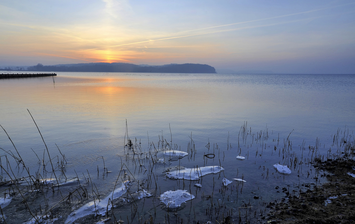 Sonnenuntergang am See mit Eis auf dem Ufer und ruhigem Wasser.