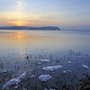 Sonnenuntergang am See mit Eis auf dem Ufer und ruhigem Wasser.