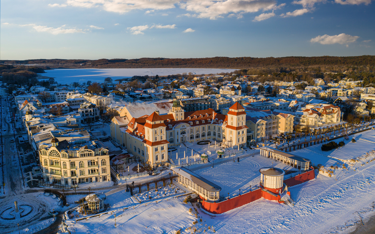 Kurhaus von Binz im Winter, umgeben von schneebedeckten Gebäuden und der gefrorenen Ostsee.