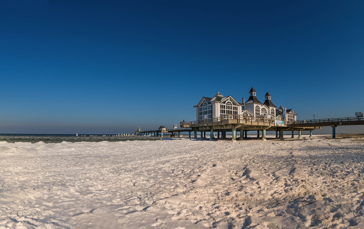 Seebrücke an einem sonnigen Tag mit klarem Himmel und Strand.