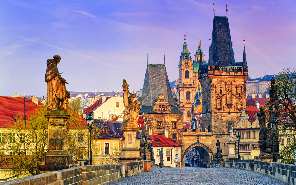 Historische Brücke mit Statuen und alten Gebäuden im Hintergrund. Prag