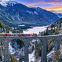Zug auf Viadukt in winterlicher Berglandschaft bei Sonnenuntergang.