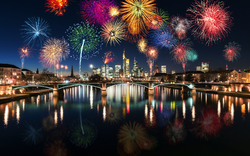 Feuerwerk über einer nächtlich beleuchteten Stadt mit Fluss und Brücke.
