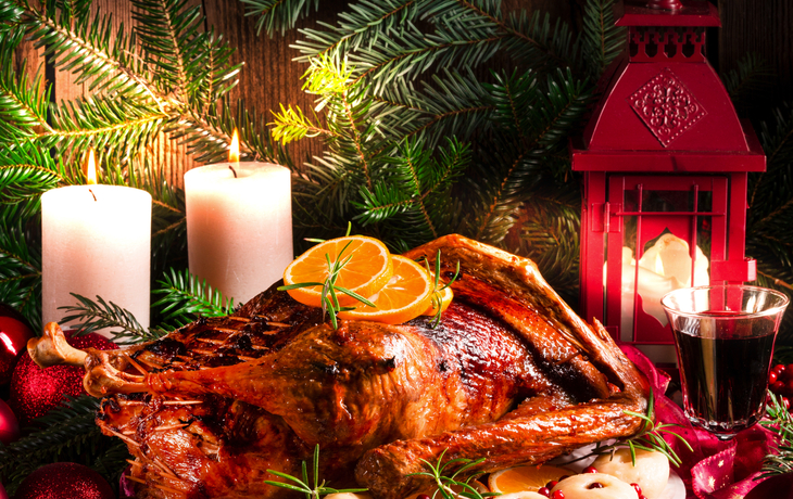 Festlich gedeckter Tisch mit gebratenem Truthahn, Kerzen und Weihnachtsschmuck.