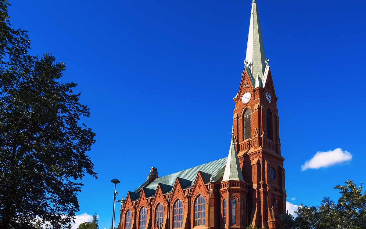 Mikkeli-Kathedrale in Finnland an einem klaren Tag mit blauem Himmel und umliegenden Bäumen.