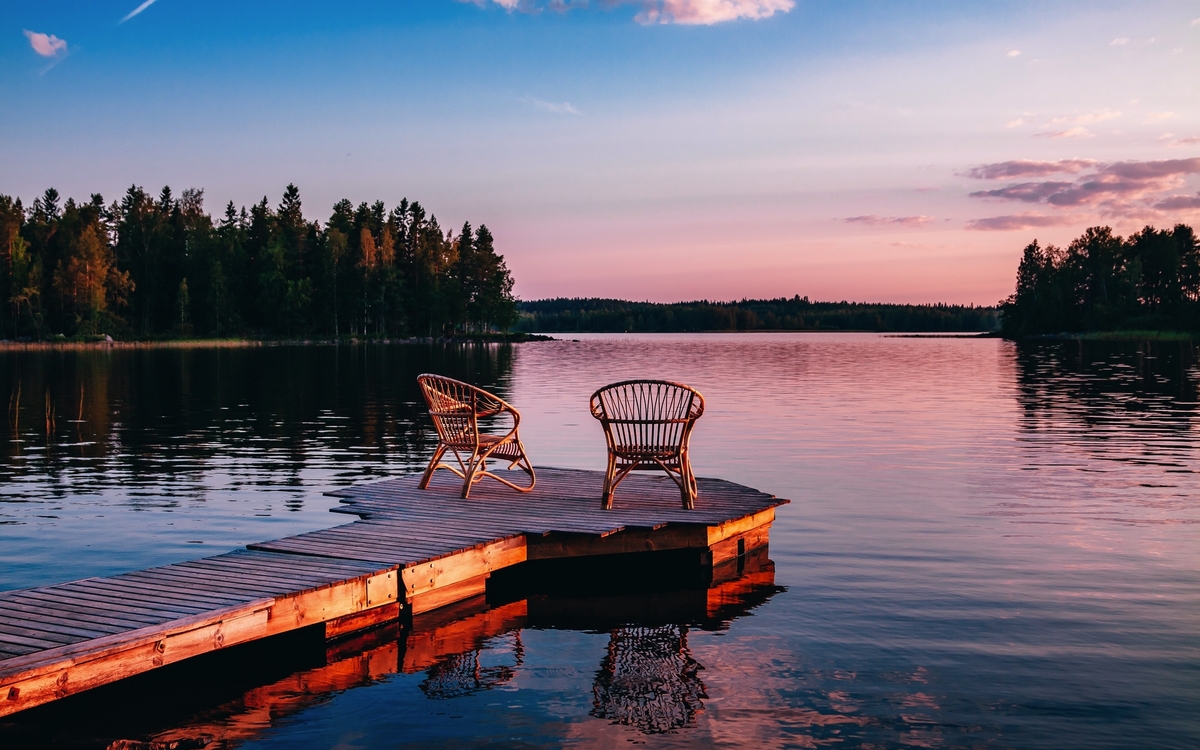 Zwei Stühle auf einem Holzsteg am See bei Sonnenuntergang.