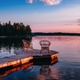Zwei Stühle auf einem Holzsteg am See bei Sonnenuntergang.
