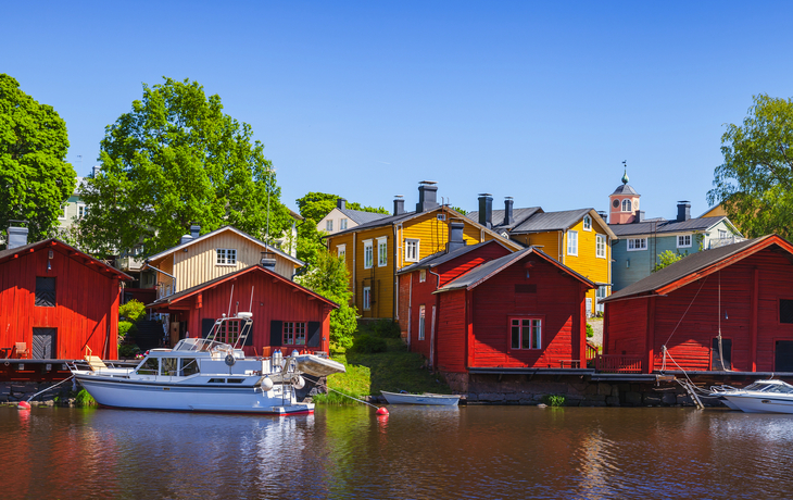 Bunte Holzhäuser am Flussufer mit Boot und blauem Himmel. Porvoo