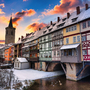 Winterliche Brücke mit Fachwerkhäusern und Kirchturm im Hintergrund bei Sonnenuntergang.