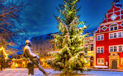 Verschneiter Platz mit Weihnachtsbaum und rotem Gebäude im Hintergrund.