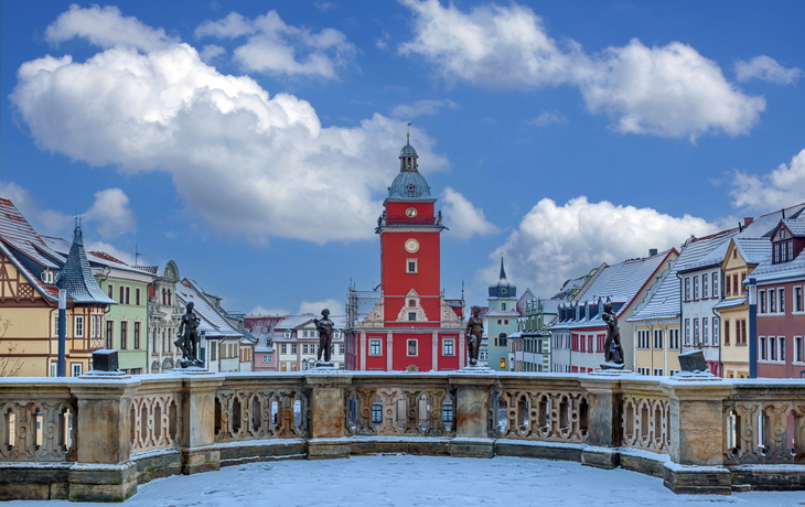 Marktplatz mit rotem Turmgebäude, umgeben von bunten Häusern im Winter.