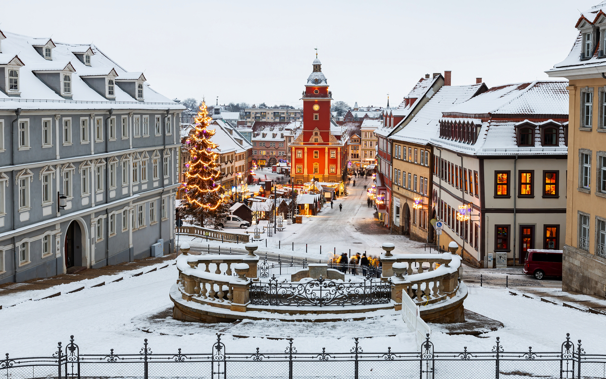 Verschneiter Marktplatz mit Weihnachtsbaum und festlich beleuchteten Gebäuden.