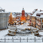Verschneiter Marktplatz mit Weihnachtsbaum und festlich beleuchteten Gebäuden.
