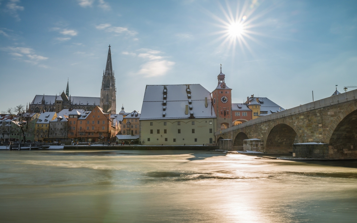 Verschneite Altstadt mit Dom und Brücke im Sonnenlicht. Regensburg