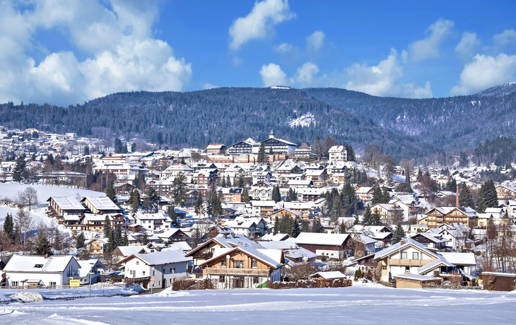 Verschneite Stadtlandschaft mit Bergen im Hintergrund.