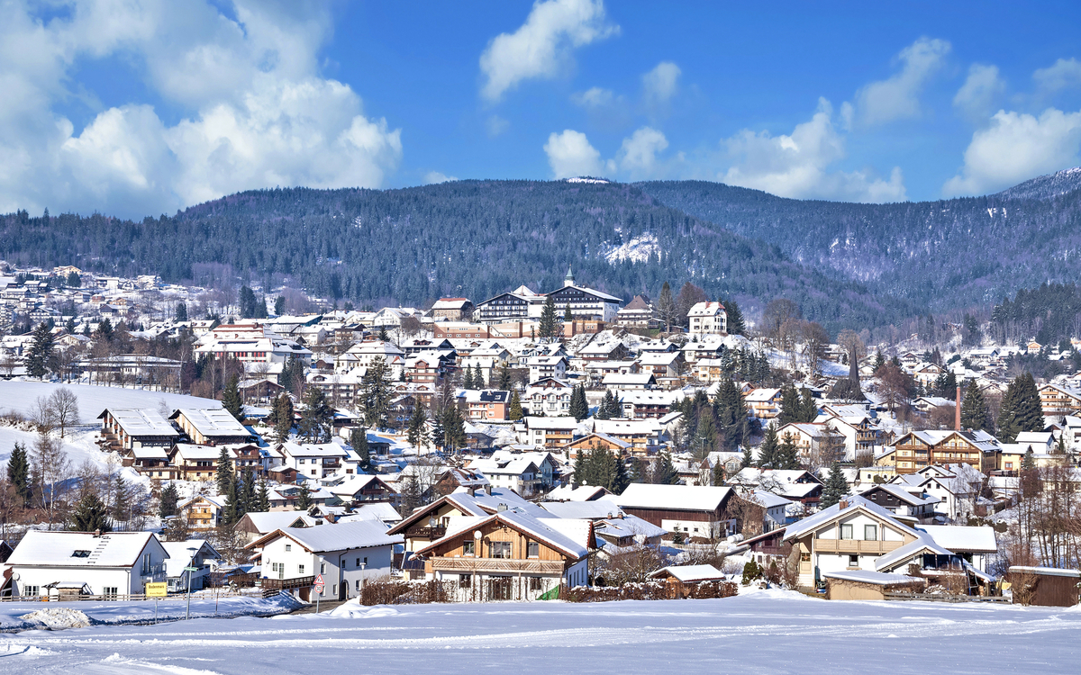 Verschneite Stadtlandschaft mit Bergen im Hintergrund.