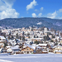 Verschneite Stadtlandschaft mit Bergen im Hintergrund.