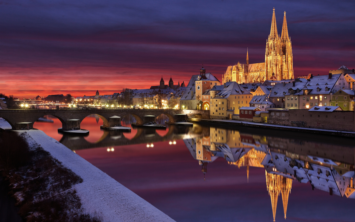Regensburg bei Sonnenuntergang mit Dom und Steinerner Brücke, Spiegelung im Fluss. Regensburg