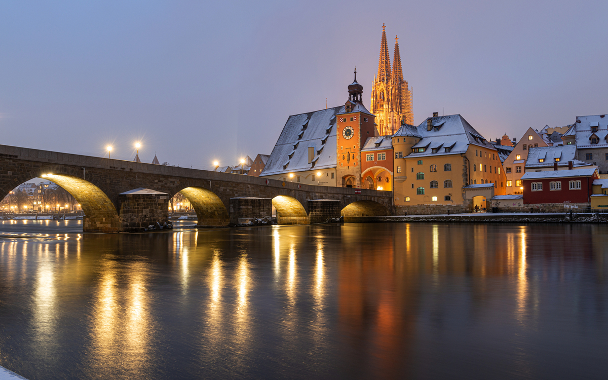 Steinbrücke und Altstadt im Winter mit beleuchtetem Kirchturm im Hintergrund Regensburg